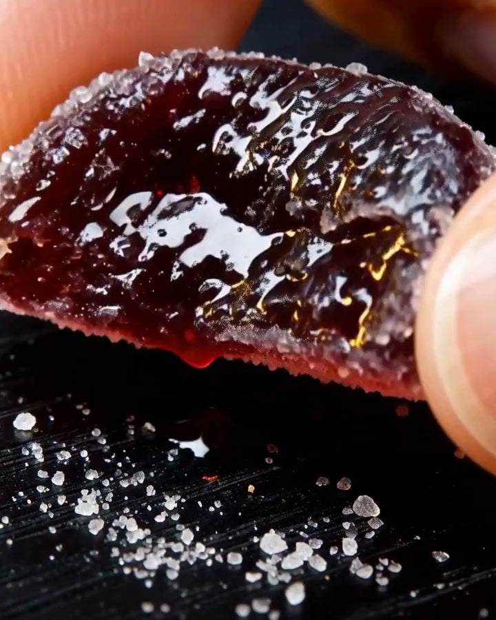 A Dandy gummy cut in half, turned slowly so its glossy berry-red center catches the light