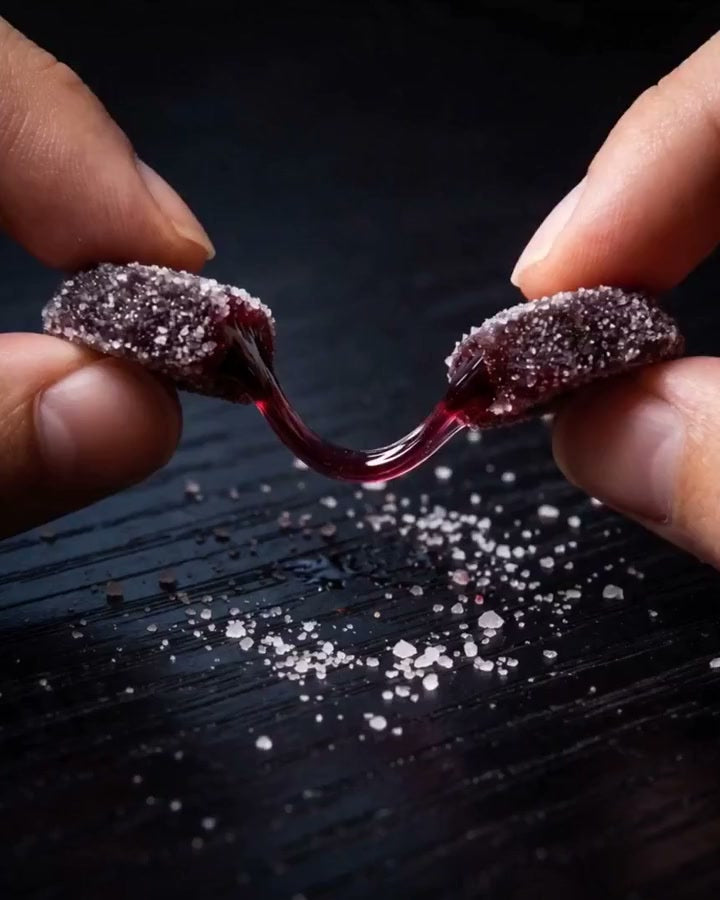 Two hands pulling a Dandy gummy apart, berry jelly stretching between the halves