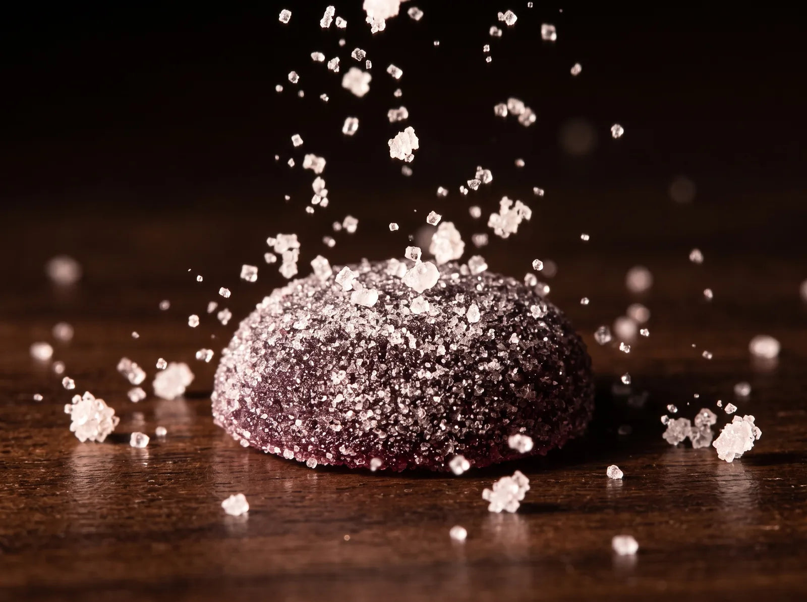 Sugar crystals landing around a Dandy gummy on dark wood