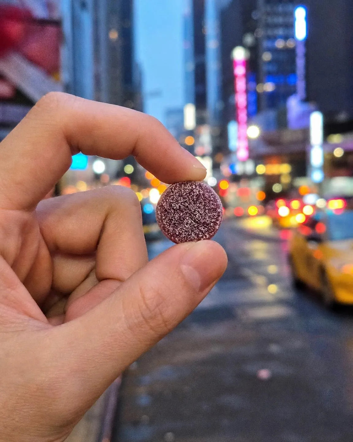 A hand holding one Dandy gummy on a city street