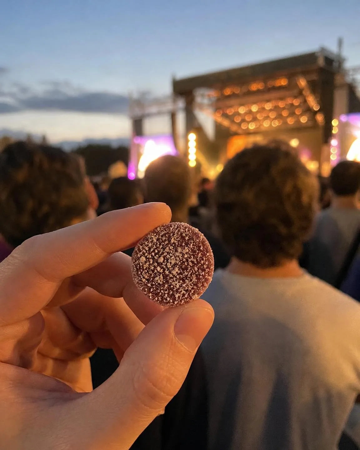 A hand holding one Dandy gummy at a concert