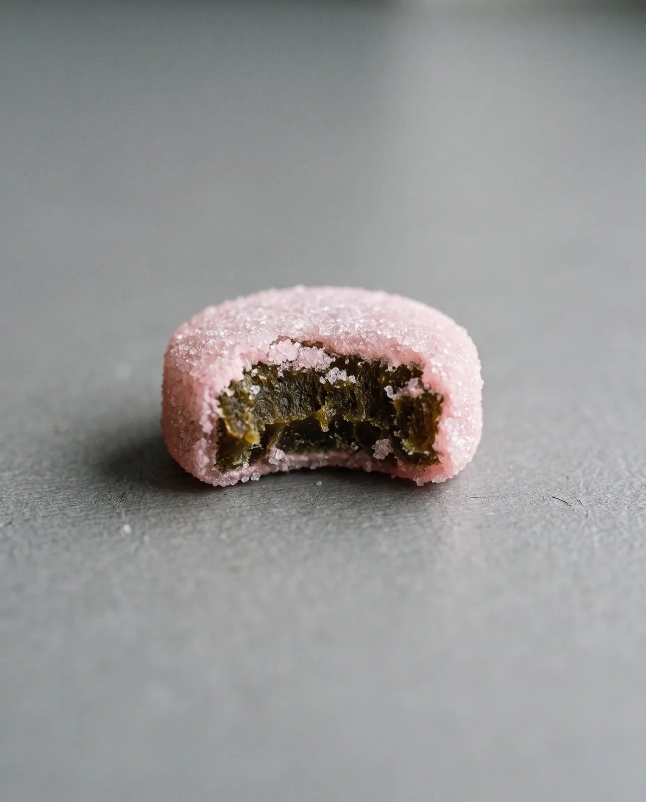 A generic sugar-shelled gummy bitten in half, a dark bitter core inside a thin sweet shell