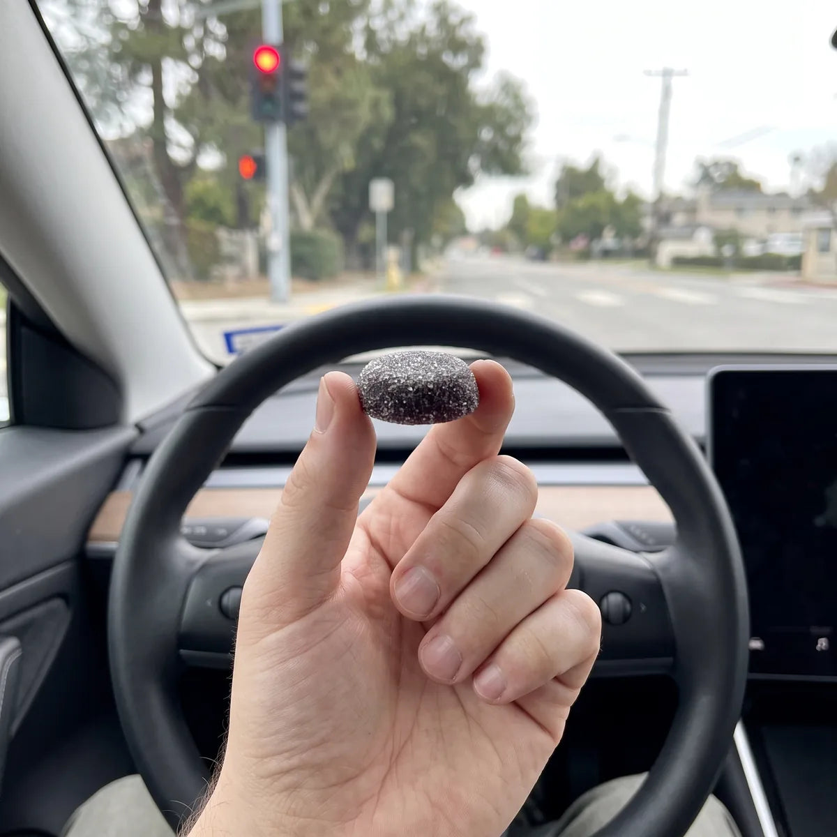 A hand holding one Dandy gummy in a car