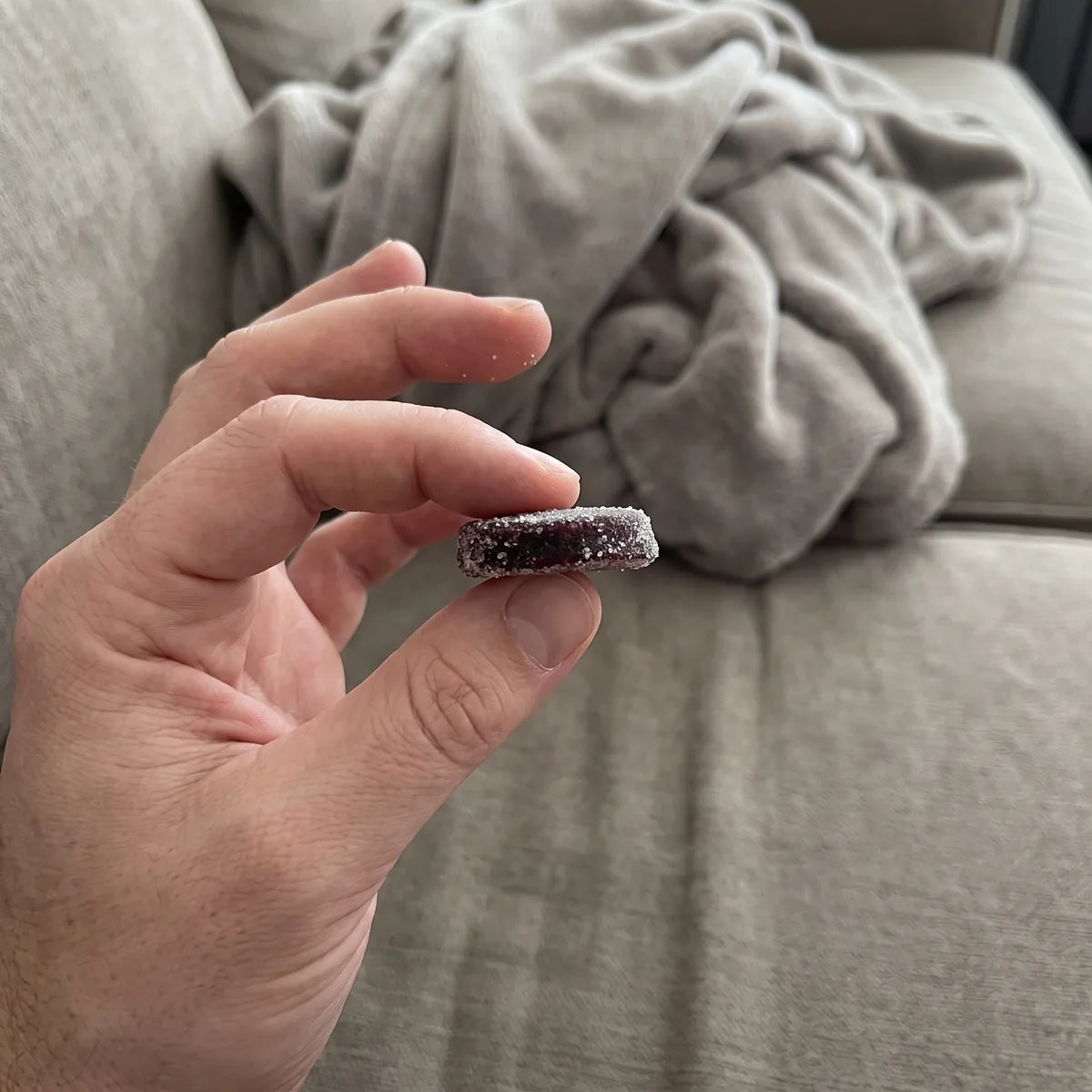 A hand holding one Dandy gummy on a couch