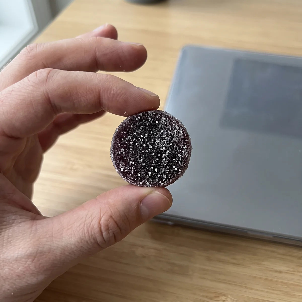 A hand holding one Dandy gummy at a desk