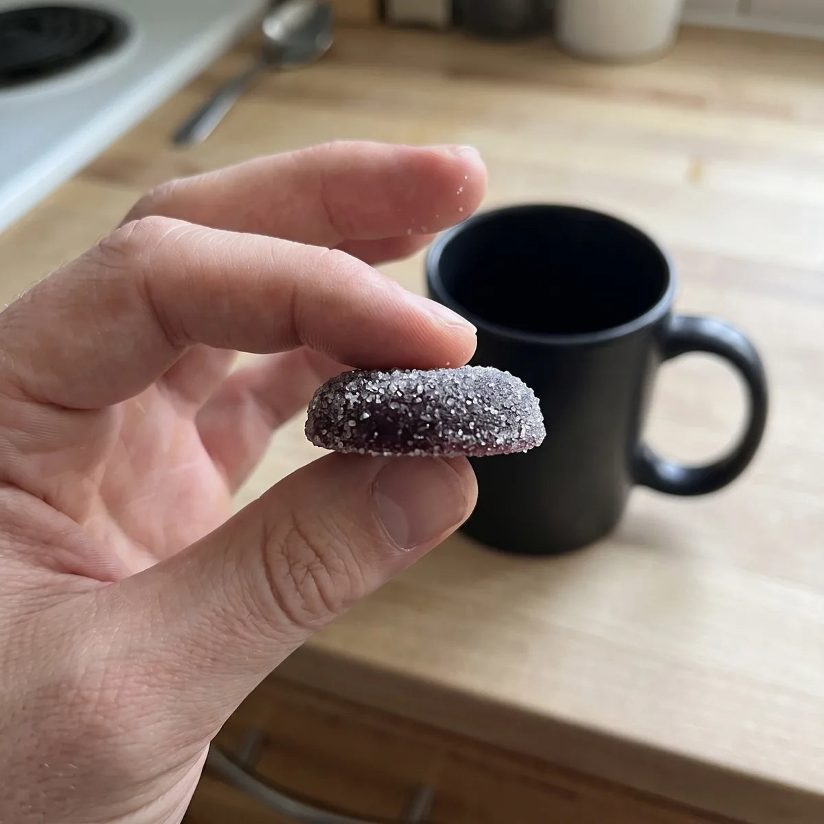 A hand holding one Dandy gummy over a kitchen counter