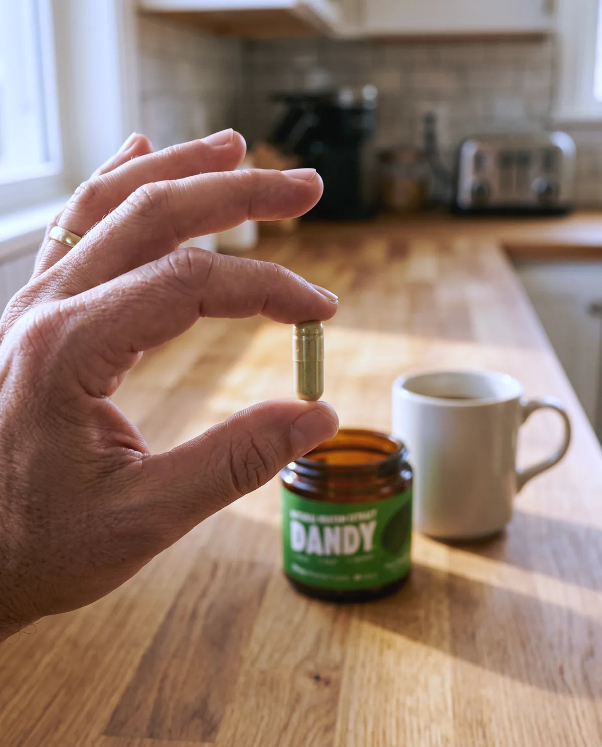 A hand holding a Dandy capsule beside its jar