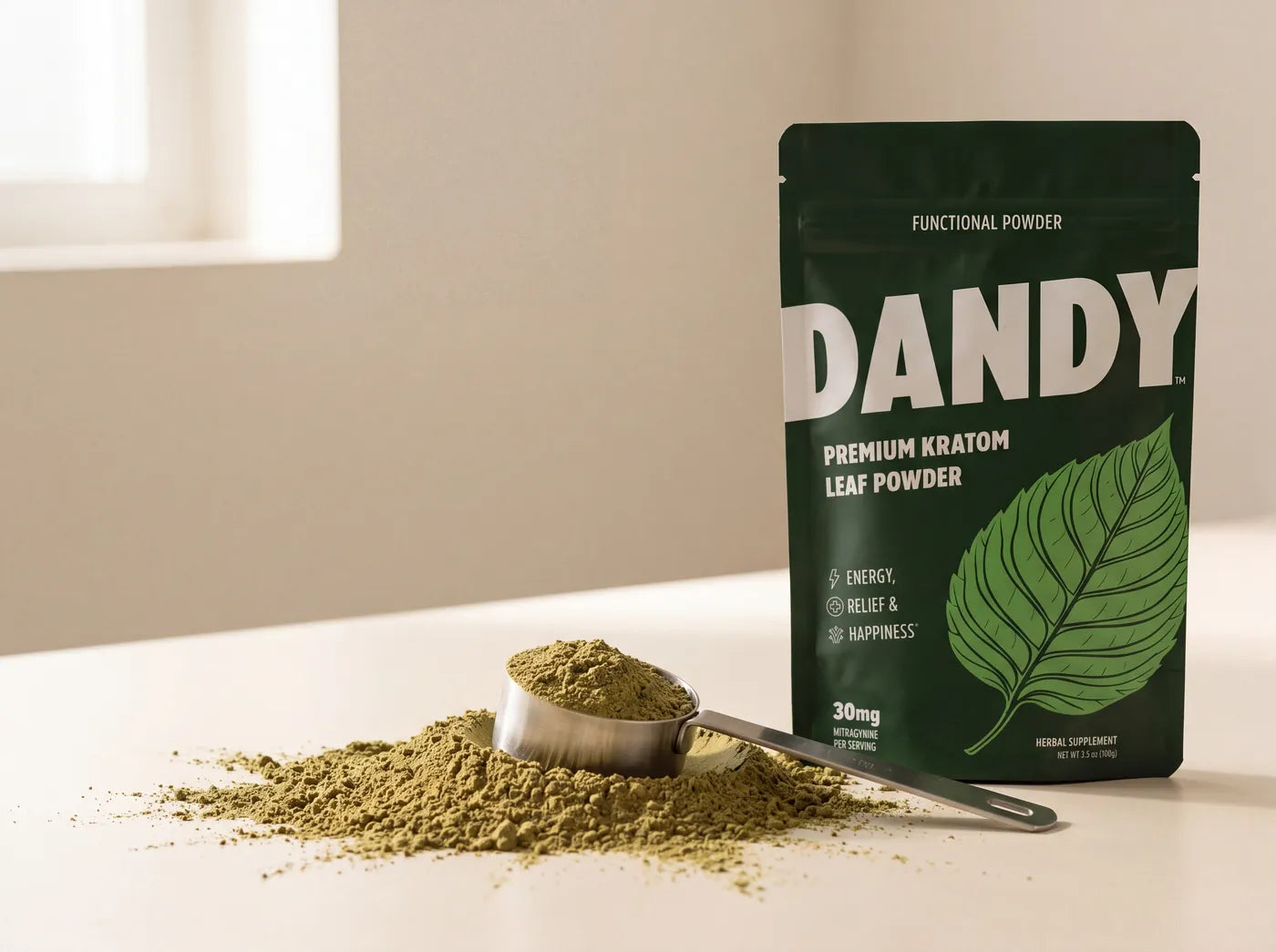 Green raw leaf kratom powder with a clean scoop beside the Dandy powder pouch.