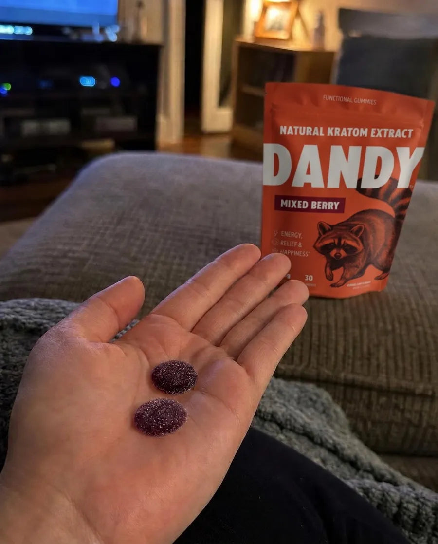 Two Dandy gummies in a customer's palm on the couch, the pouch beside them.
